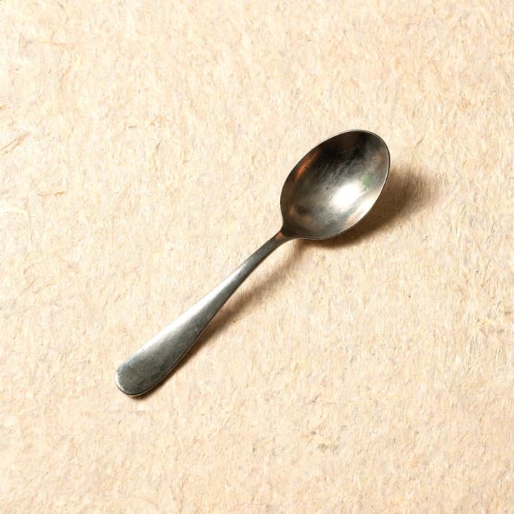 A well-used tasting spoon, photographed on bone-coloured paper.