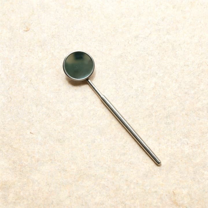 A well-used dentist's mirror, photographed on bone-coloured paper.