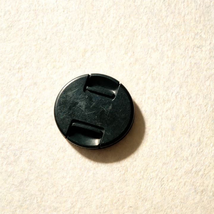 A well-used lens cap, photographed on bone-coloured paper.