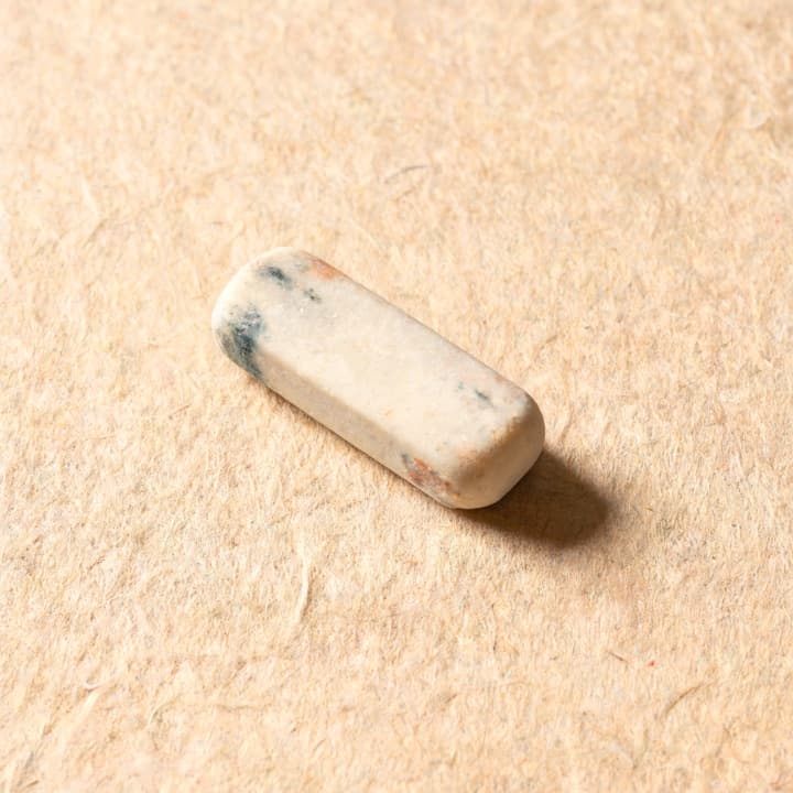 A well-used tailor's chalk, photographed on bone-coloured paper.